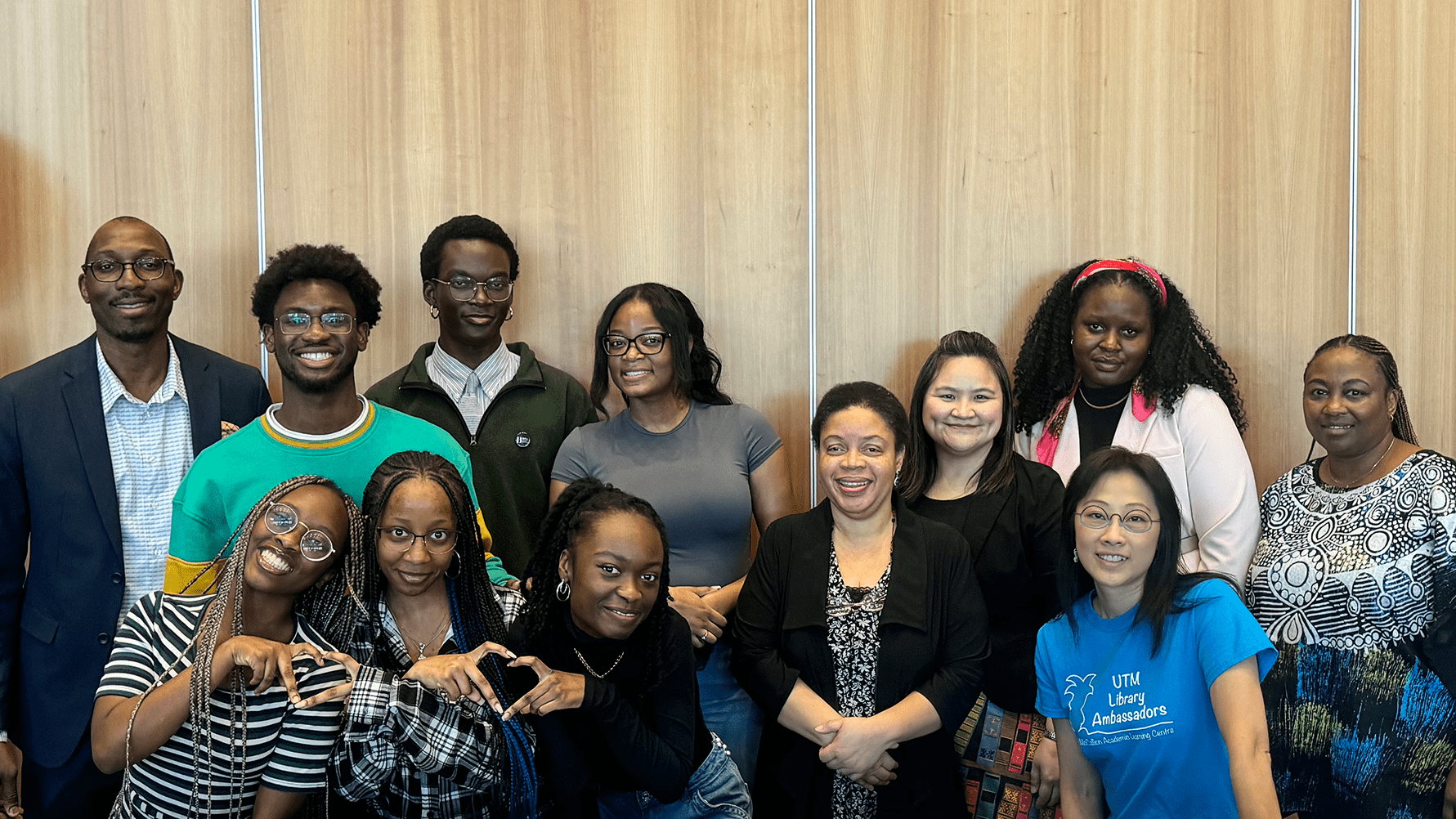Group of Staff and Students Posing Together Against a Wooden Panel