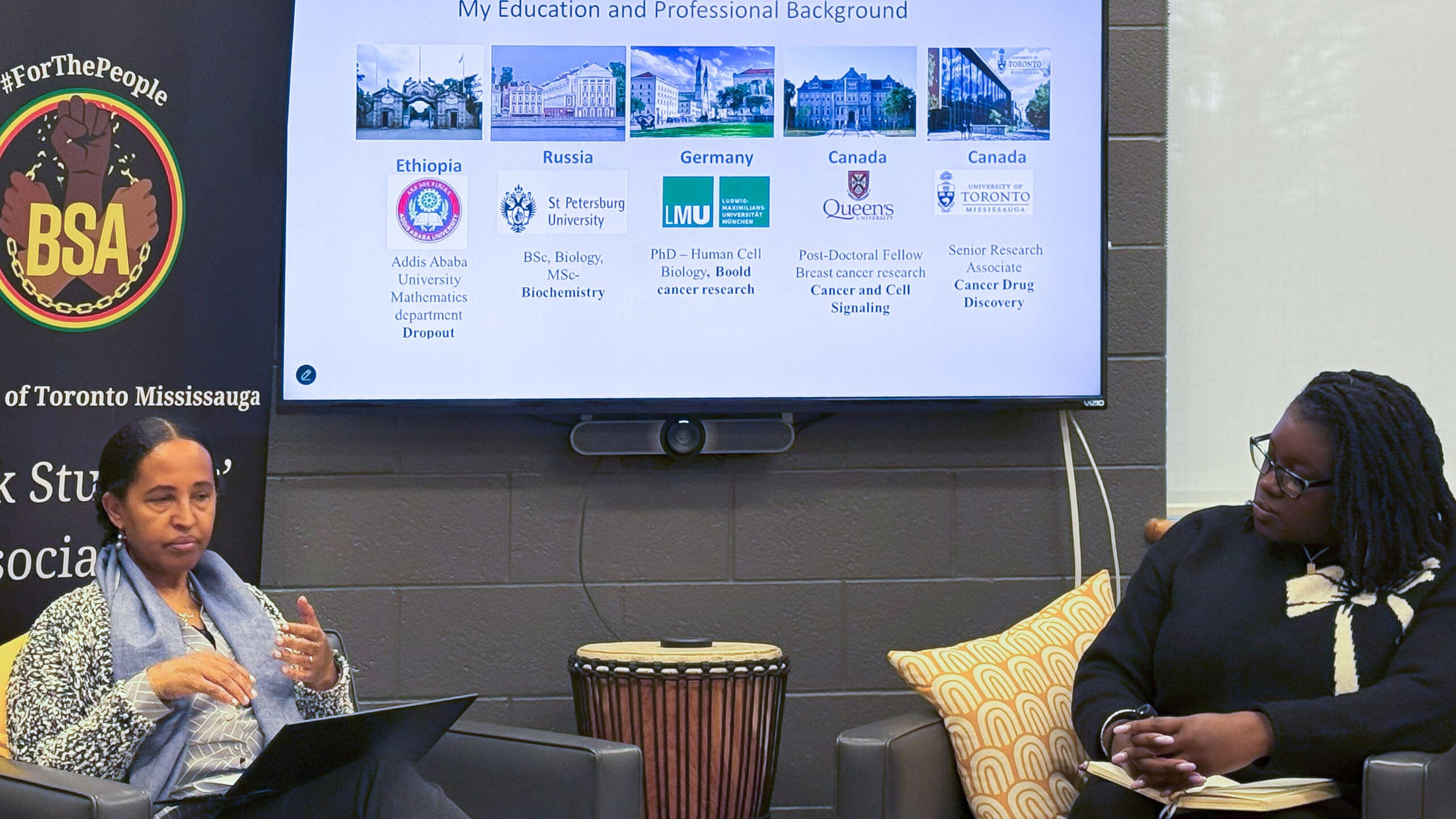 A panel speaker seated in front of a screen with a guest